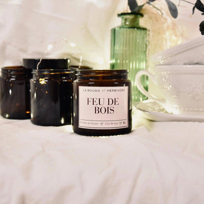 Bougie parfumée feu de bois de La Bougie Herbivore avec un pot en verre brun sur un fond doux